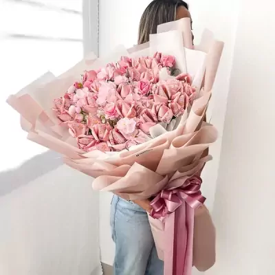 Pink money bouquet with artificial flowers and pink ribbon, held by a person in jeans.