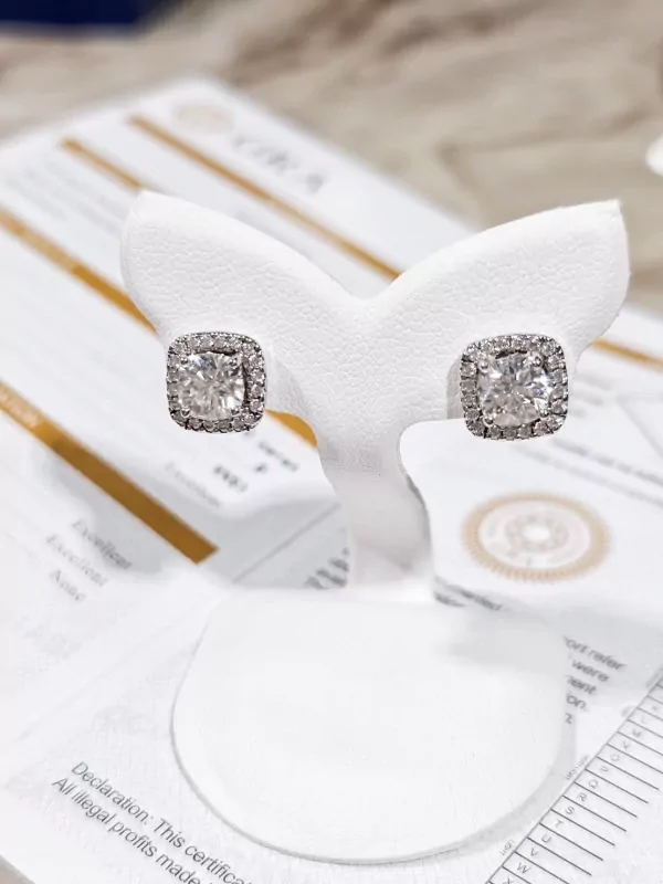 Cushion-cut moissanite diamond earrings in a halo setting, displayed on a white stand.