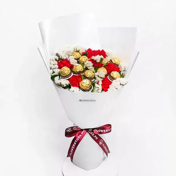 Bouquet of red carnations, white statice, and Ferrero Rocher chocolates wrapped in white paper with a burgundy ribbon.