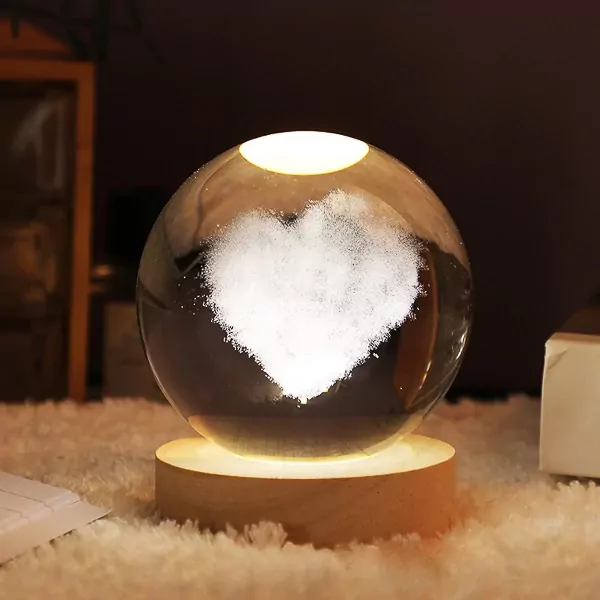 Crystal ball lamp with a 3D carved heart inside, on a wooden base, illuminated with warm LED light.