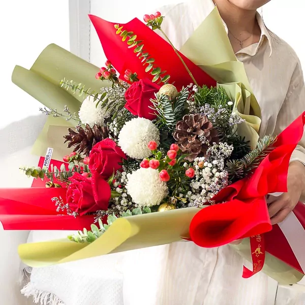 A festive bouquet with red roses, white ping pong flowers, pine cones, and red berries.