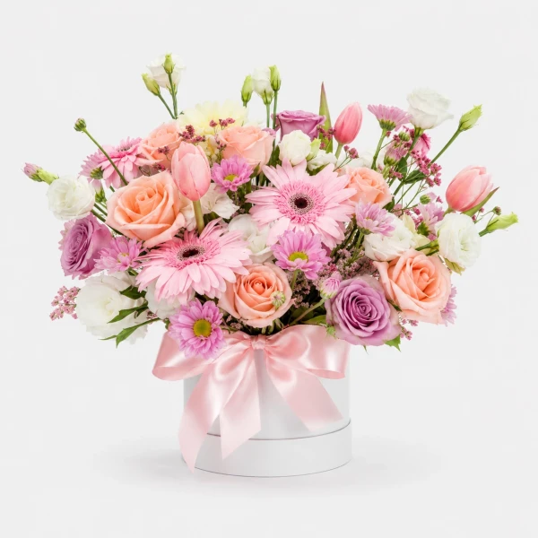 Pink and peach roses, pink gerbera daisies, and purple mums in a white vase with a pink bow.