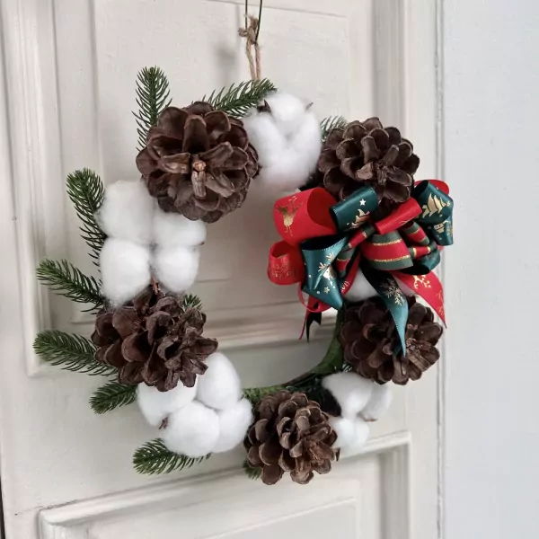 Christmas wreath with pine cones, cotton, greenery, and a festive red and green bow.