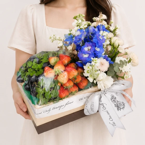 Fruit and flower gift box with strawberries, grapes, blue and white flowers, and a ribbon.