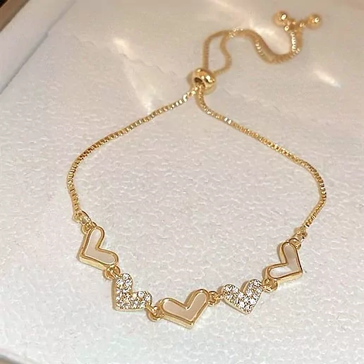 Gold chain bracelet with five heart charms, some inlaid with white material and others with small stones.