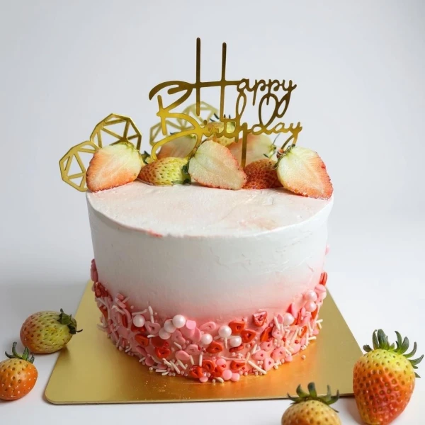 A round, pink and white tres leches cake topped with sliced strawberries and a "Happy Birthday" topper.