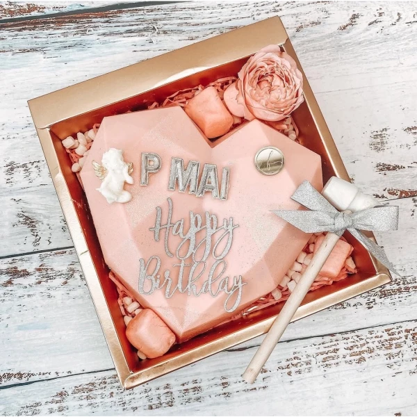 Pink heart-shaped chocolate gift box with "Happy Birthday" and "P MAI" in silver, a small hammer, and pink candy.
