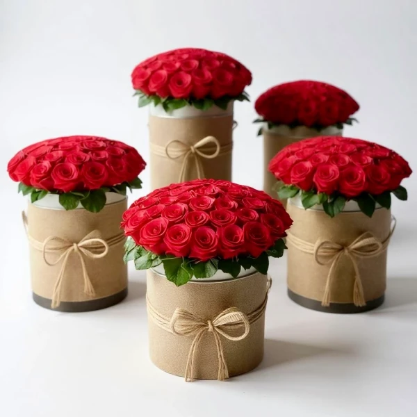 Five round boxes of red roses, some tied with twine, arranged on a white surface.