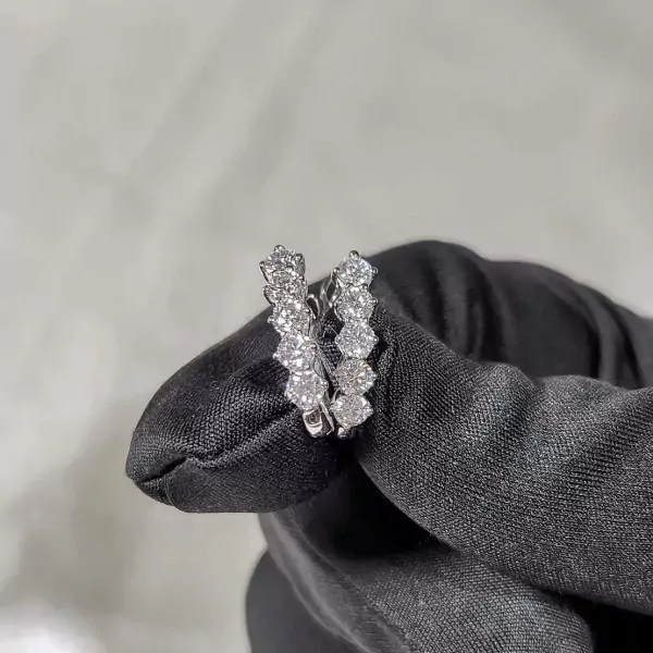 Diamond-encrusted hoop earrings held by a black gloved hand.