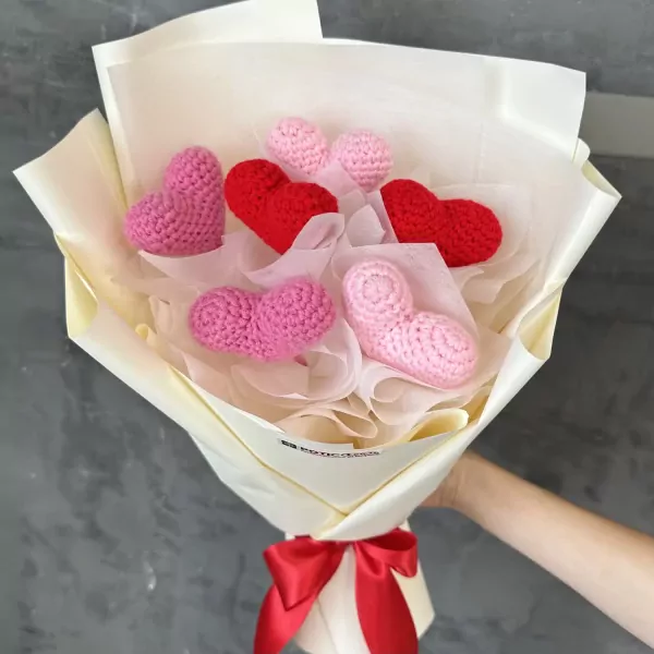 Crocheted heart bouquet in shades of pink and red, wrapped in cream paper with a red ribbon.