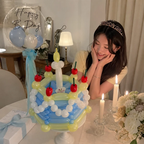 A blue and yellow balloon cake with white balloon accents, red cherries, green stems, and yellow candle balloons on a white stand.