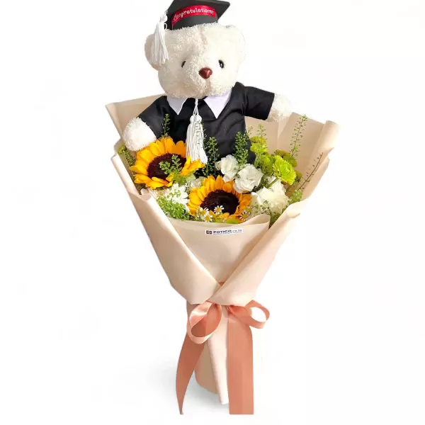 White graduation teddy bear in a bouquet of sunflowers, white flowers, and greenery.