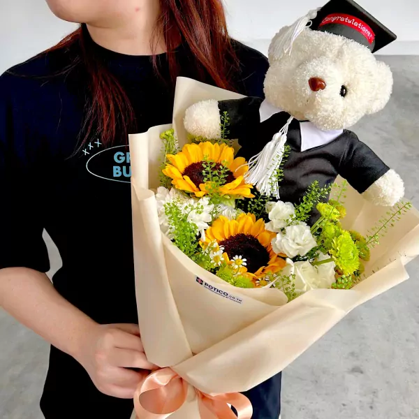 Graduation teddy bear bouquet with sunflowers and white flowers, wrapped in beige paper.