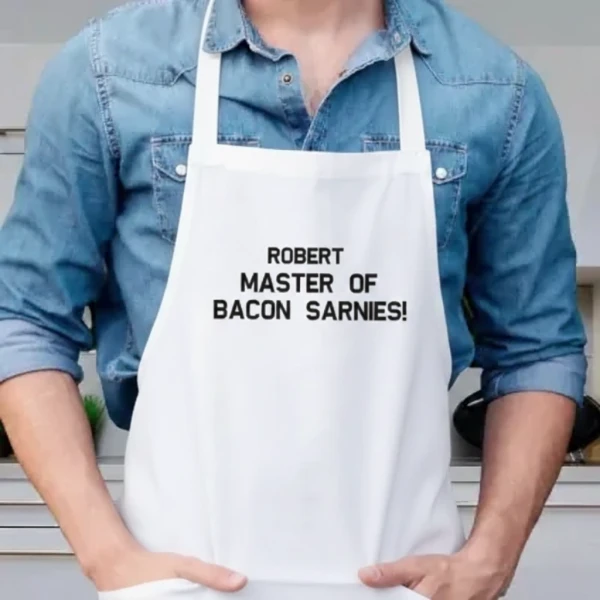 White apron with black text "ROBERT MASTER OF BACON SARNIES!" on it.
