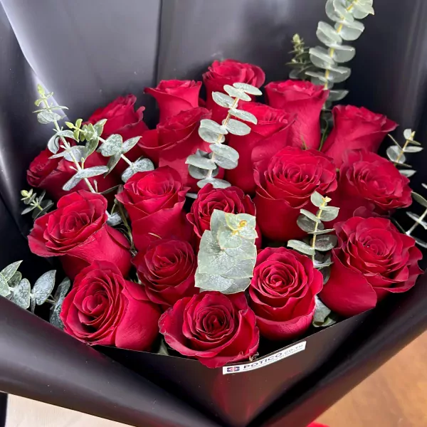 A bouquet of 18 vibrant red roses with eucalyptus, wrapped in black paper.