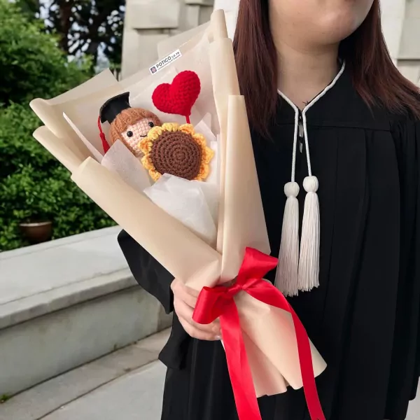 Crocheted graduation bouquet with sunflower and heart, held by a person in academic regalia.