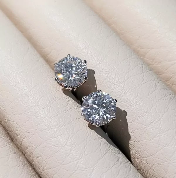 Two round-cut moissanite diamond solitaire earrings on a textured surface.