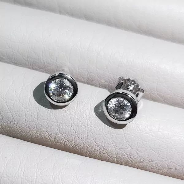 Pair of 0.5-carat round-cut moissanite diamond earrings set in silver with a white textured background.