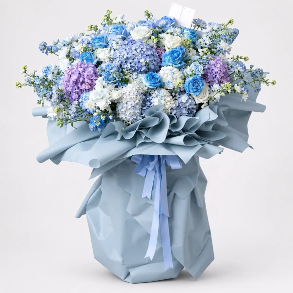 Luxury Ocean Dreams Bouquet: blue hydrangeas, roses, and white flowers wrapped in blue paper, tied with a blue ribbon.