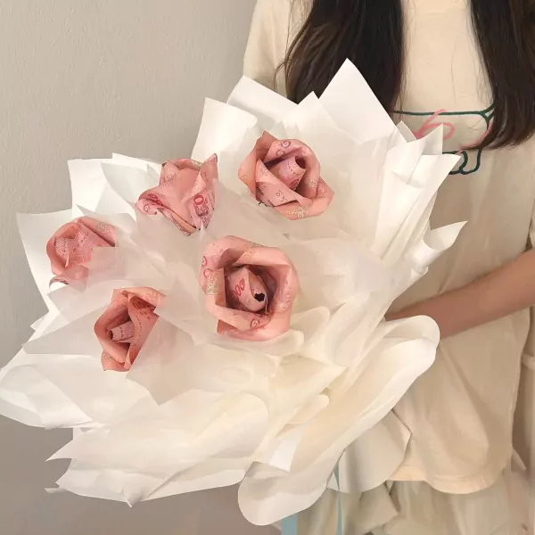Bouquet of five pink roses made from rolled banknotes, wrapped in white tissue paper.