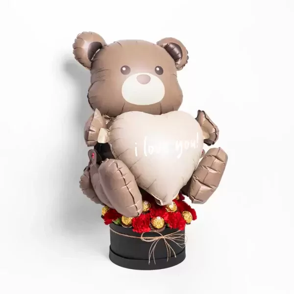 A teddy bear balloon holds a heart that says "I love you," surrounded by red carnations and chocolates.