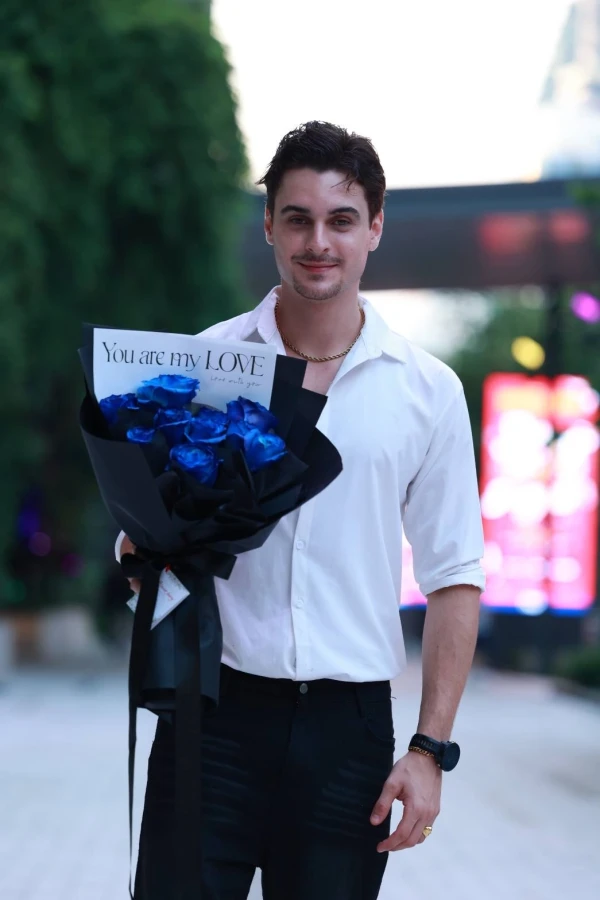 Man holding a bouquet of blue roses in black wrapping with a card that says "You are my LOVE".