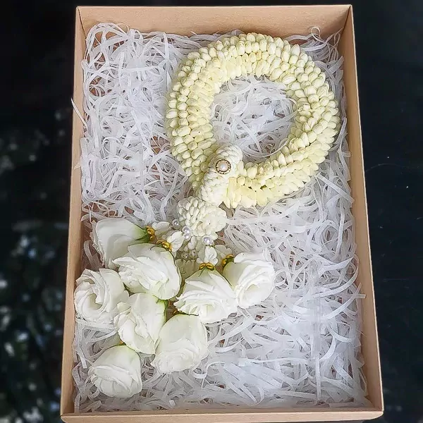 White fresh malai with jasmine and roses in a box lined with white paper shred.