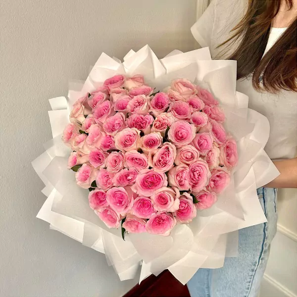 A large bouquet of 50 vibrant pink roses wrapped in white paper, held by a person.