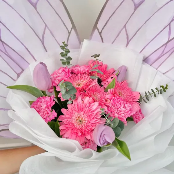 Pink gerbera daisies, carnations, and purple tulips arranged in a bouquet with butterfly-wing-inspired wrapping.