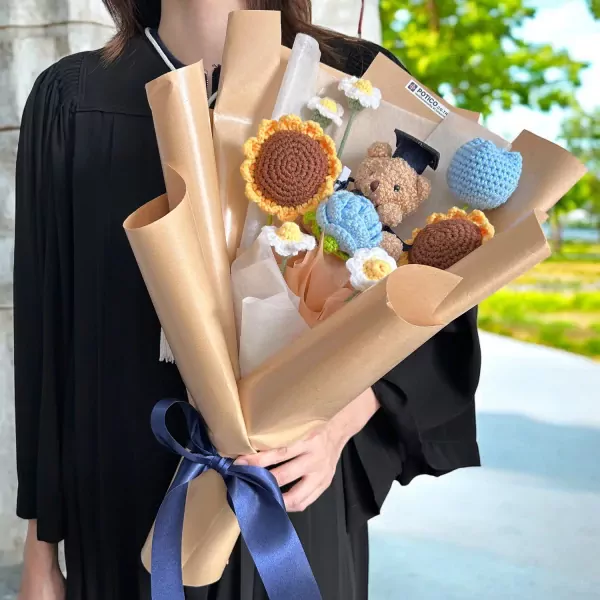 Crochet graduation bouquet with teddy bear, sunflowers, and daisies, tied with a blue ribbon.