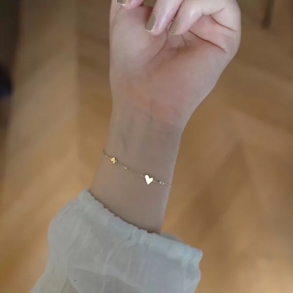 Gold dainty heart bracelet on a wrist wearing a white shirt.