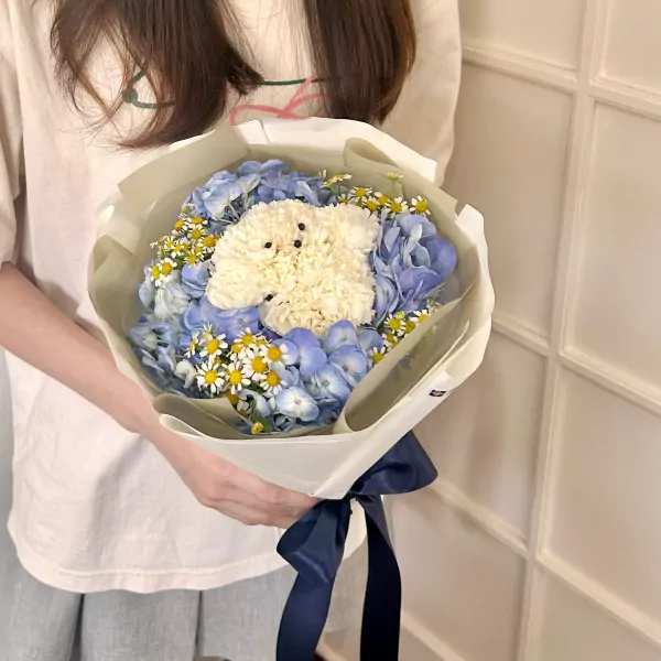 Bouquet with blue hydrangeas, daisies, and a white floral dog in the center, tied with a navy ribbon.