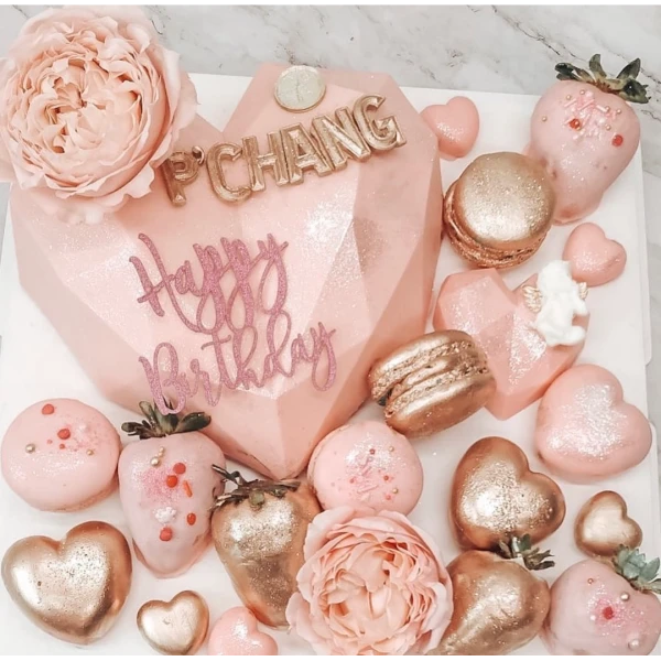 Pink heart-shaped chocolate gift box with gold "P CHANG" and "Happy Birthday" decorations, surrounded by macarons and chocolate-covered strawberries.