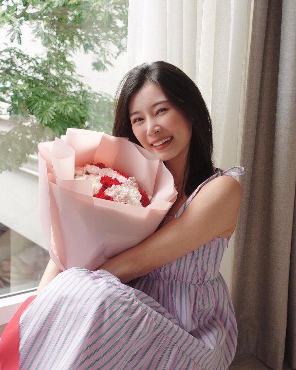 A young woman with dark hair smiles holding a pink bouquet of carnations.