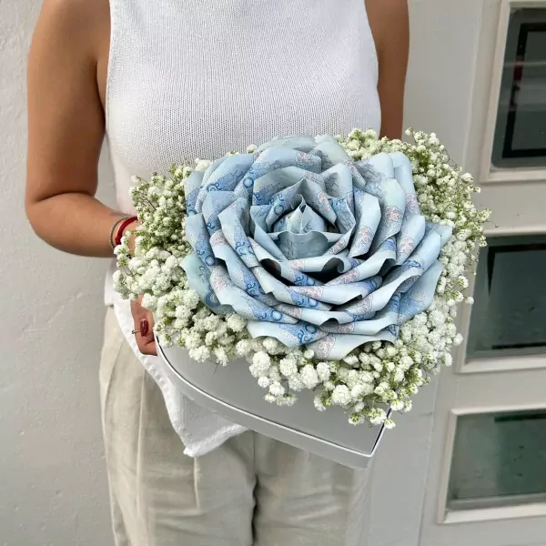 A heart-shaped box filled with baby's breath and a large rose made of blue banknotes.