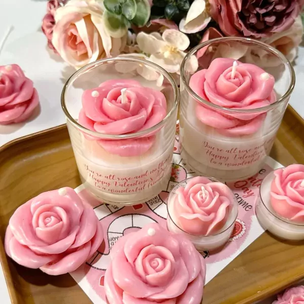 Pink rose candles in glass jars and small votives on a wooden tray, with pink flowers in the background.
