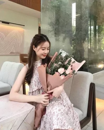 Woman in floral dress holding a pink rose and eucalyptus bouquet.