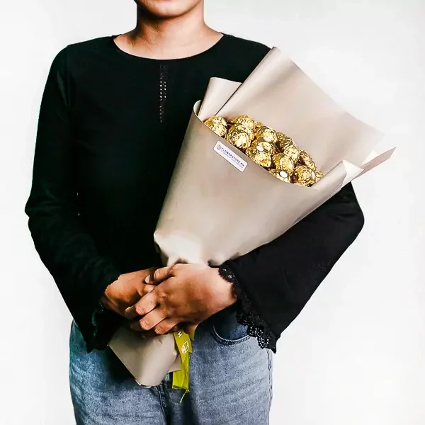 A person holds a bouquet of 22 Ferrero Rocher chocolates wrapped in beige paper.