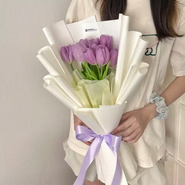 A bouquet of purple tulips wrapped in white paper with a purple ribbon.