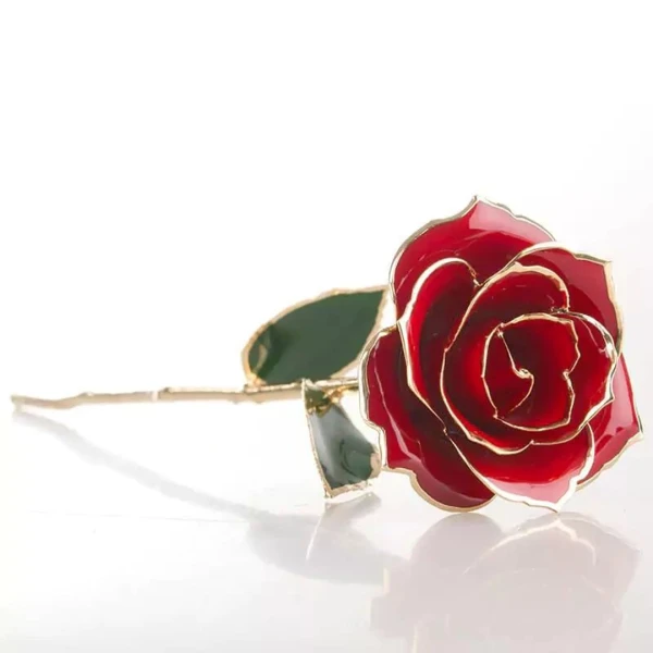 A red rose dipped in 24K gold with a gold stem and green leaves on a white background.