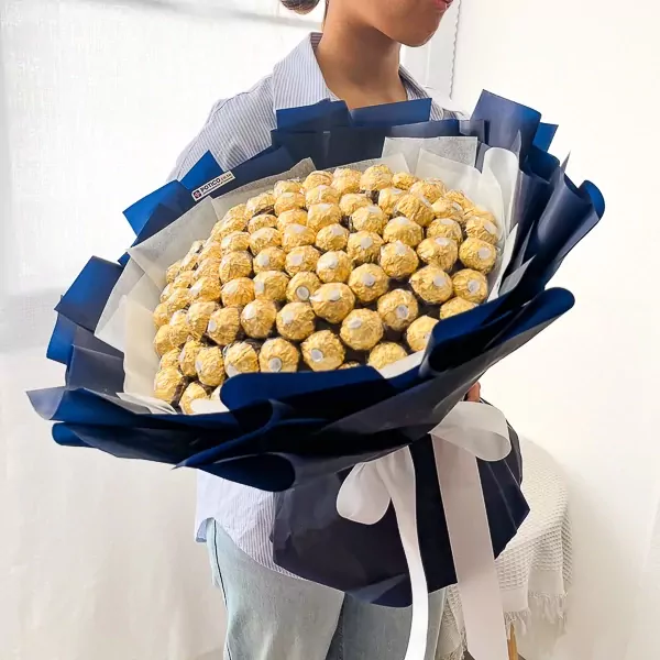 A person holds a large bouquet made of 100 Ferrero Rocher chocolates wrapped in navy blue and white paper.