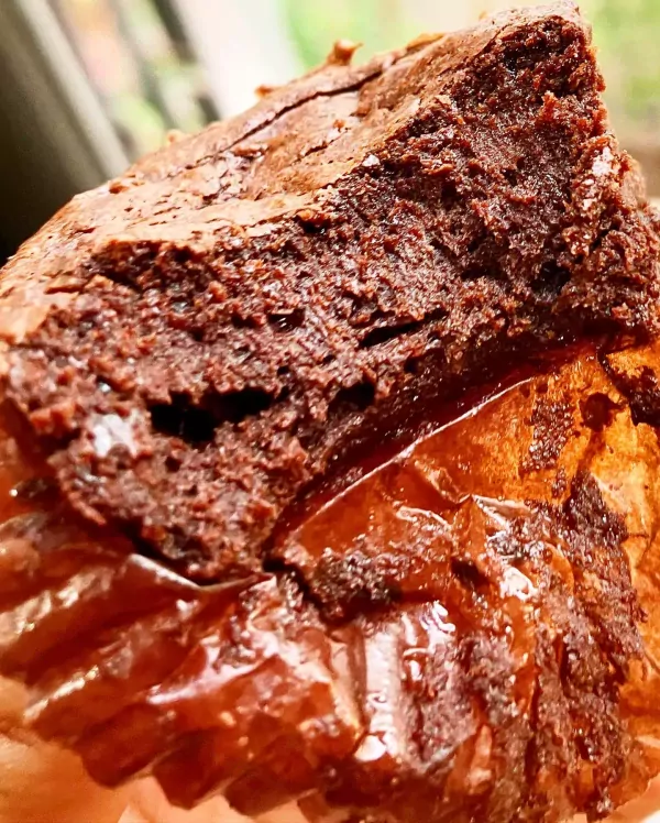 Close-up of a rich, dark chocolate brownie with a fudgy texture, sitting in a wrapper.