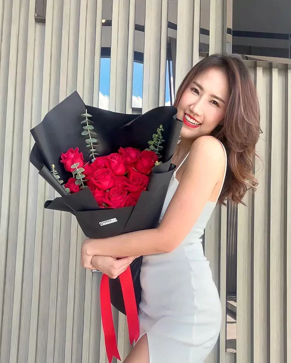 Woman holding a bouquet of 18 red roses wrapped in black paper.
