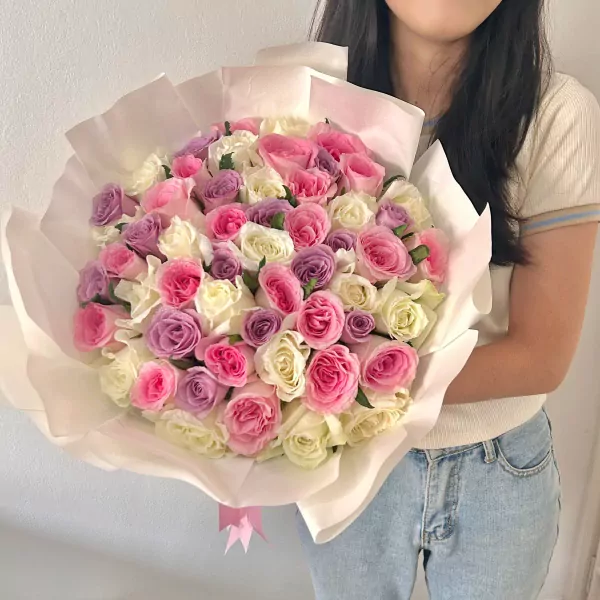 A large bouquet of 50 pink, purple, and white roses, held by a person in a white top and jeans.