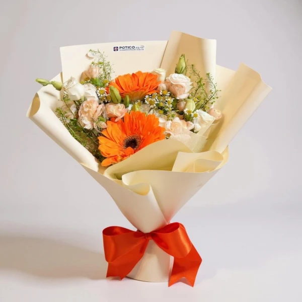 Bouquet of orange gerberas, white roses, and small white flowers wrapped in cream paper with an orange ribbon.