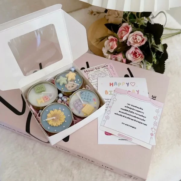 Four decorative scented candles in round metal tins, in a gift box with a birthday card and flowers.
