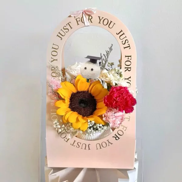 Pink graduation bloom basket with sunflower, carnation, roses, and graduation bear.