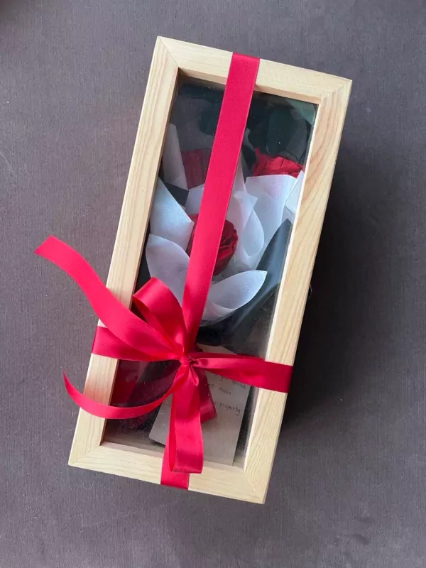 Wooden box with three preserved red and white roses, tied with a red ribbon.