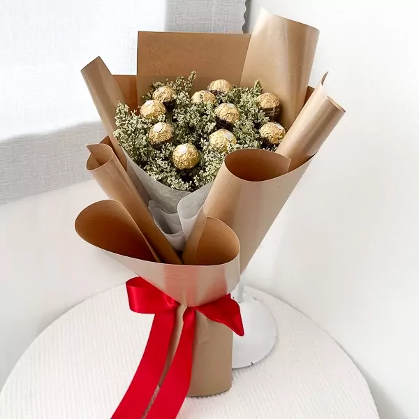 Ferrero Rocher and dried yellow limonium flowers bouquet wrapped in brown paper, tied with red ribbon.