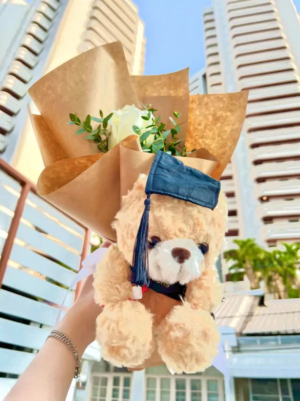 Graduation teddy bear with white rose bouquet, wrapped in brown paper.